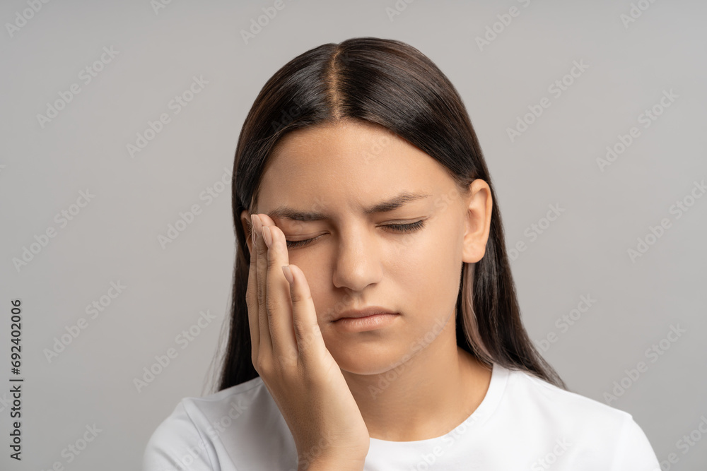 Overworked stressed tired teenage girl with closed eyes, touching head, feeling uncomfortable painful pressure, strain in temples, dizziness. Exhausted teenager in need of medical treatment and rest Overworked stressed tired teenage girl with closed eyes, touching head, feeling uncomfortable painful pressure, strain in temples, dizziness. Exhausted teenager in need of medical treatment and rest