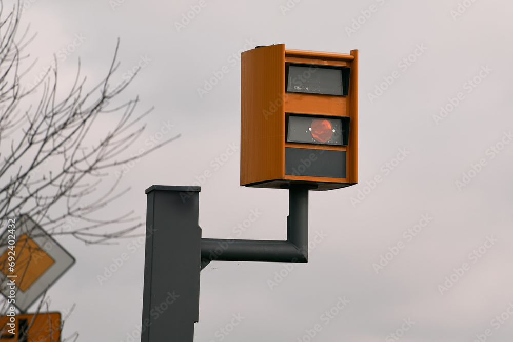 A yellow speed camera flashes as it detects a speeding car on a highway