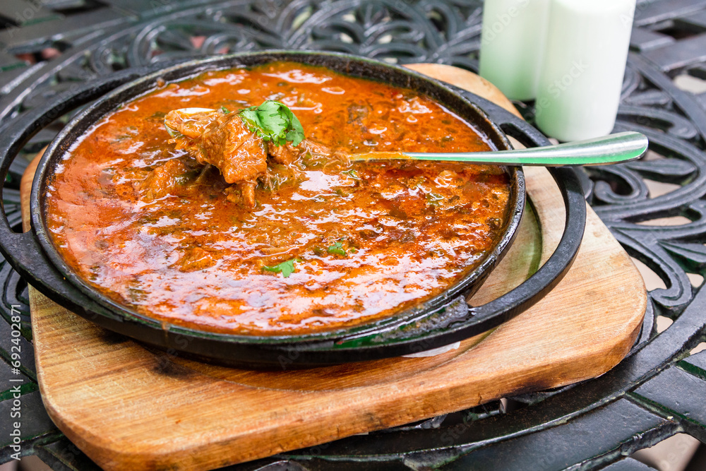 travel to Georgia - eating of Georgian dish Ostri (stewed pieces of meat in sauce with Georgian spices) in pan in local outdoor cafe in Tbilisi city - obrazy, fototapety, plakaty 