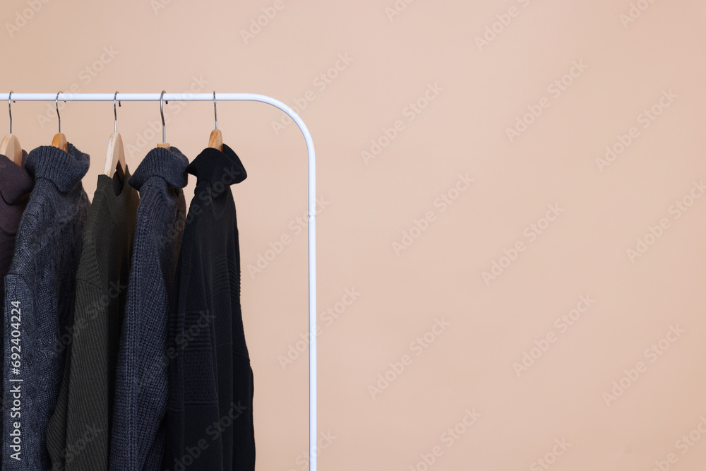 Rack with different warm sweaters on beige background. Space for text Rack with different warm sweaters on beige background. Space for text