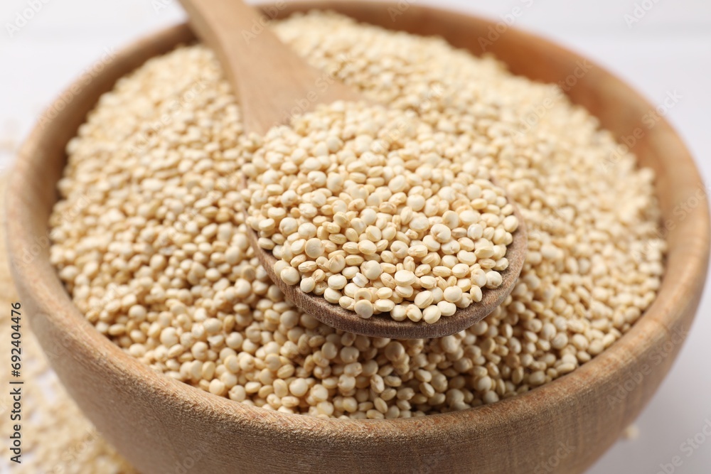 Dry quinoa seeds and spoon in bowl on white table, closeup Dry quinoa seeds and spoon in bowl on white table, closeup