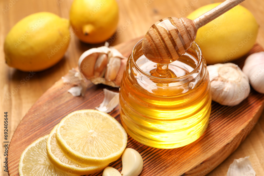 Pouring honey from dipper into jar, garlic and lemons on wooden table, closeup Pouring honey from dipper into jar, garlic and lemons on wooden table, closeup