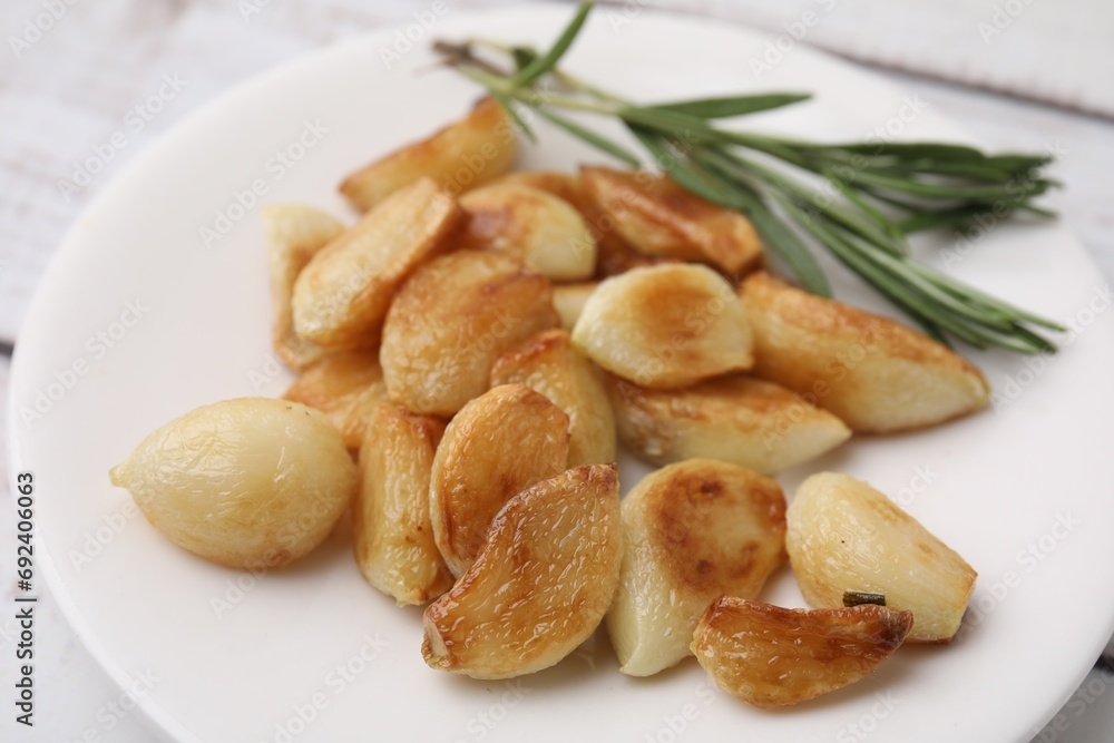 Fototapeta premium Fried garlic cloves and rosemary on plate, closeup