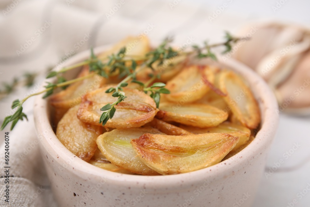 Fried garlic cloves and thyme in bowl on table, closeup