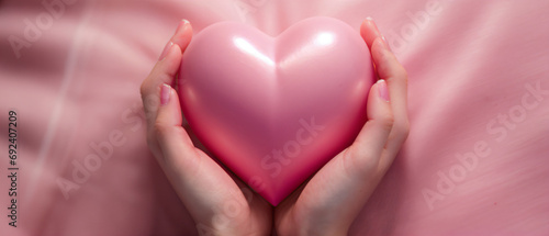 Hand holding pink heart on pink backgroud.