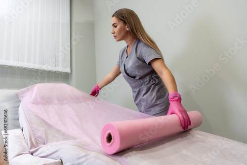 Foto Woman cosmetologist spreads disposable bedspread on couch for cosmetic procedure