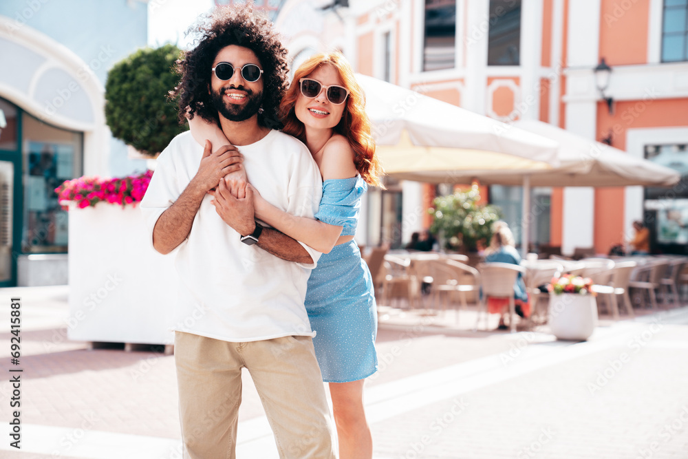 Smiling beautiful redhead  woman and her handsome boyfriend. Model in casual summer clothes. Happy cheerful family. Female having fun. Couple posing in the street at sunny day, in sunglasses
