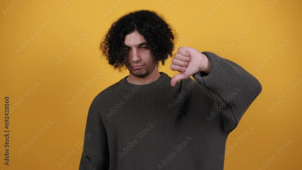 Dislike. Upset unhappy man showing thumbs down sign gesture, expressing discontent, disapproval, dissatisfied negative feedback. Curly man indoors isolated on yellow background. Lifestyle. Emotions Dislike. Upset unhappy man showing thumbs down sign gesture, expressing discontent, disapproval, dissatisfied negative feedback. Curly man indoors isolated on yellow background. Lifestyle. Emotions