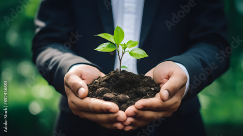 Hands of a businessman holding with care the seedling of a plant with green leaves sprouting. Sustainable growth & environmentally conscious long term investment concept.