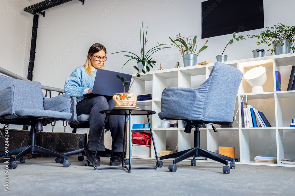 Young women sitting in coworking space working while using laptop. Young women sitting in coworking space working while using laptop.