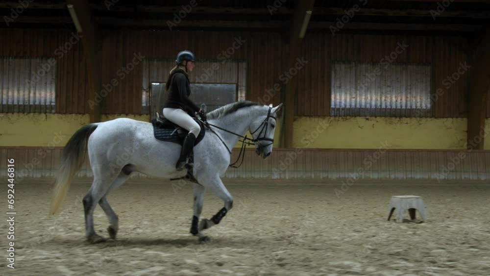 A white horse with a female rider trotting in a barn - Slow motion shot. A white horse with a female rider trotting in a barn - Slow motion shot.
