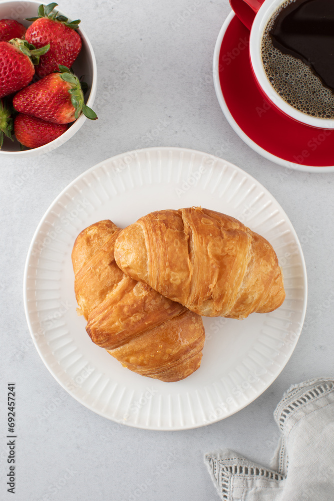 A fresh croissant with fresh strawberries and coffee. Croissant with black coffee. A fresh croissant with fresh strawberries and coffee. Croissant with black coffee.