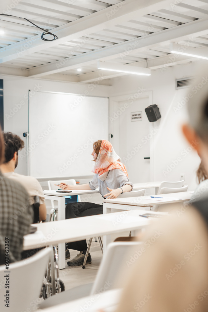 Asking questions in the middle of the presentation. Female employee wearing hijab discussing with her business trainer at the classroom Asking questions in the middle of the presentation. Female employee wearing hijab discussing with her business trainer at the classroom