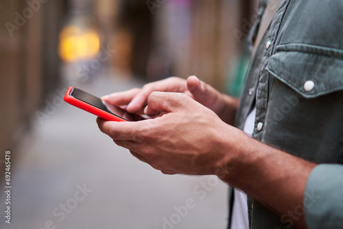 Close-up side view of the hands of an unrecognizable man holding and using a mobile phone outdoors scrolling and texting in social networks. Technology addiction.