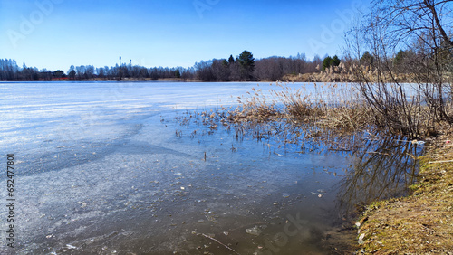 Landscape with a lake covered with ice before the start of melting and ice drift on a spring day with the sun. Blue ice and water under sunlight in early spring or autumn © keleny