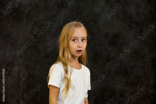 Portrait of confused girl child model in white t-shirt expression emotion, scared looking away. Anxious cover kid 6 year old posing at black, studio shot. Kids emotional concept. Copy ad text space