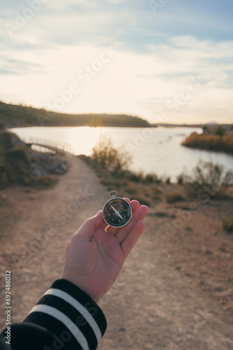 A hand holds a compass with a landscape with a lagoon in the background