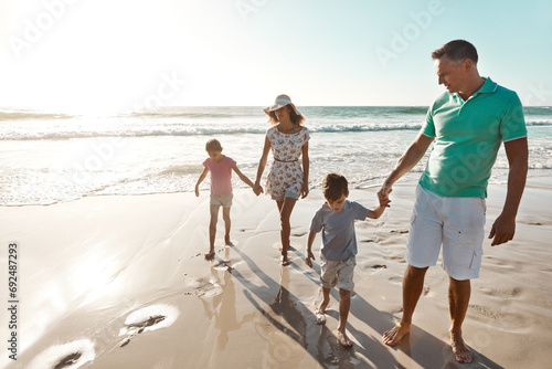 Parents, children and beach or holding hands for happy summer or travel, ocean sunshine or sibling development. Man, woman and kids on sand for holiday relax walking or outdoor, clean air or vacation photo