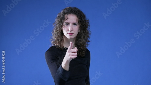 Foto Woman accusing viewer by pointing finger at camera while standing on blue background