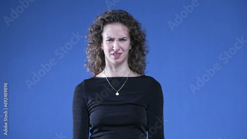 Fotografie Woman reacting with disgust and dislike looking at camera while standing on blue background