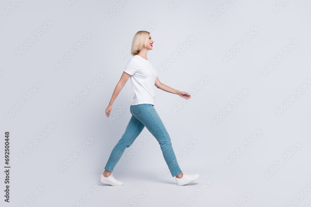 Fototapeta premium Full length photo of good mood gorgeous girl dressed white t-shirt denim pants walk look at empty space isolated on gray color background