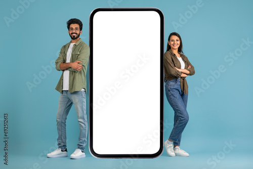 Positive young indian couple standing by big cell phone, mockup