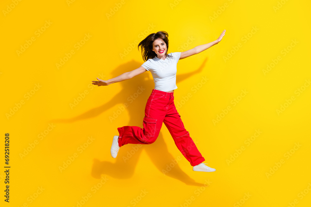 Full length photo of cool carefree lady wear white t-shirt jumping high flying arms sides isolated yellow color background Full length photo of cool carefree lady wear white t-shirt jumping high flying arms sides isolated yellow color background