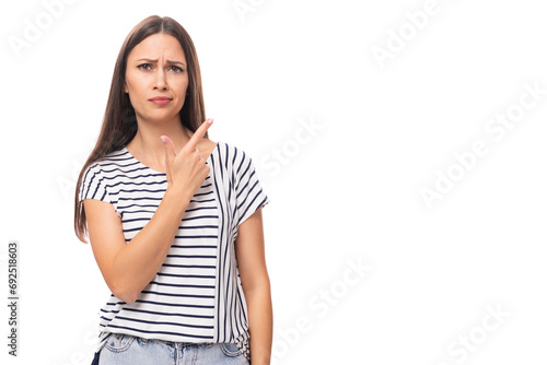 young positive pretty european brunette woman in a striped t-shirt points her finger on a white background with copy space