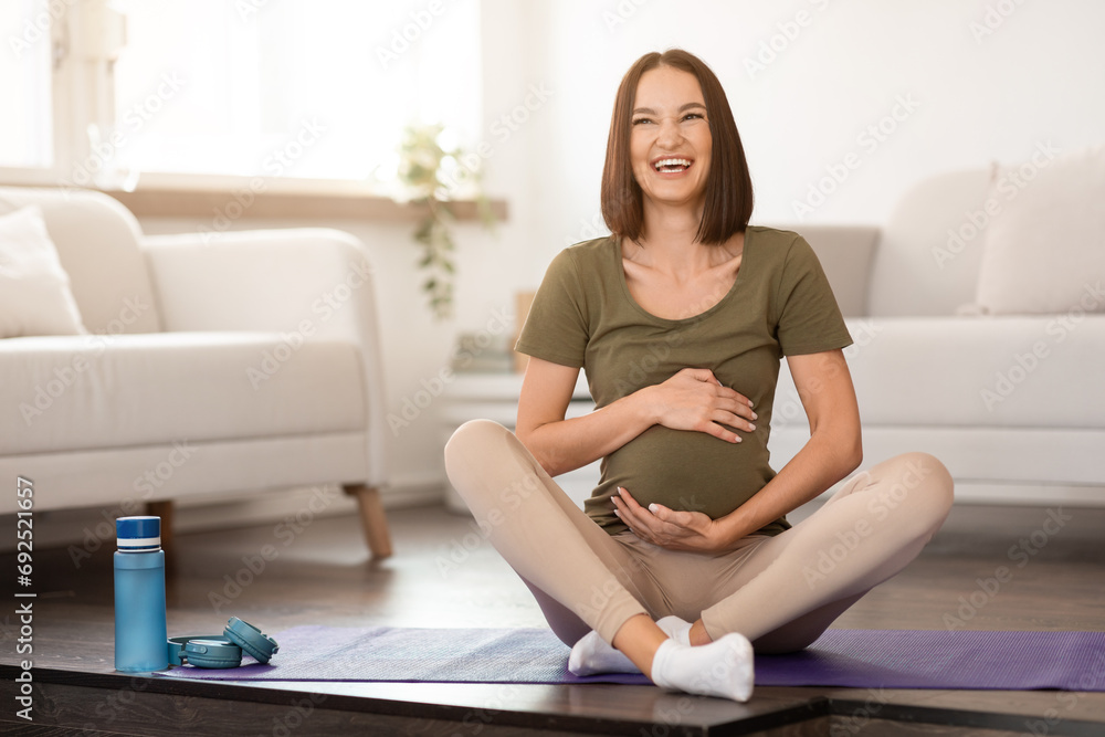 pregnant lady sits on yoga mat at home, hugging tummy pregnant lady sits on yoga mat at home, hugging tummy