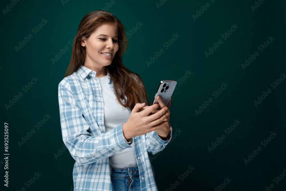 A pretty young woman with brown eyes dressed in a checkered blue shirt is chatting on a smartphone A pretty young woman with brown eyes dressed in a checkered blue shirt is chatting on a smartphone
