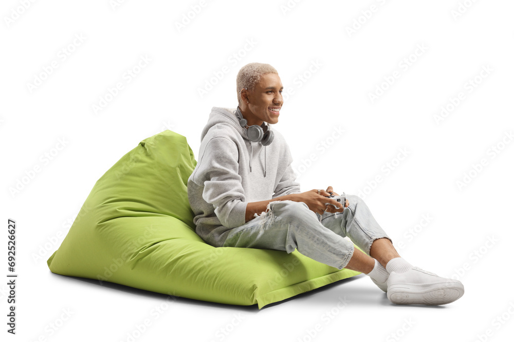 African american guy sitting on a green bean bag armchair and playing a game with joystick