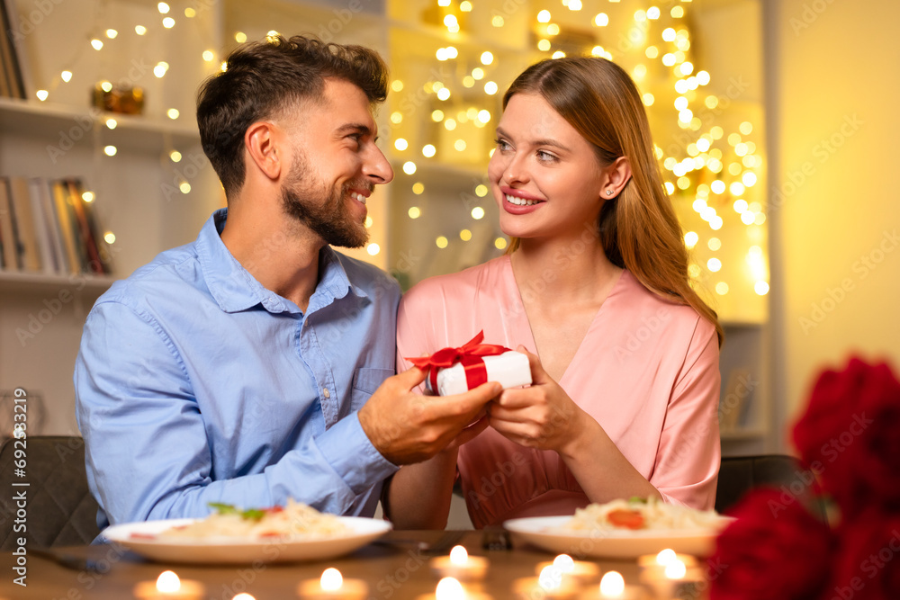 Man presents gift to woman, sharing a joyful moment at dinner Man presents gift to woman, sharing a joyful moment at dinner