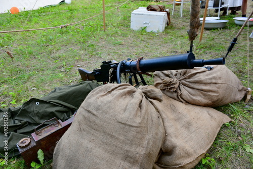 A close up on a machine gun replica from World War I seen next to some sandbags and ammo crates spotted next to a camp seen on a cloudy summer day during a historic reenactment in Poland