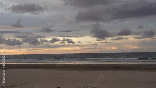 Sunset on a tropical beach. The waves of the ocean roll onto the shore. The sun has disappeared. Twilight.  The sky is painted in gold and pink colors. Pale purple clouds. Reflection on wet sand.