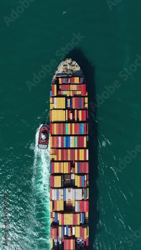 Large Container Ship and Tug Boat in Sea. Aerial Top-Down View. Freighter is Passing By. Vertical Video photo