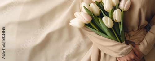 flat lay with female hands holding bunch of tulips on cream, beige textile background #692568616