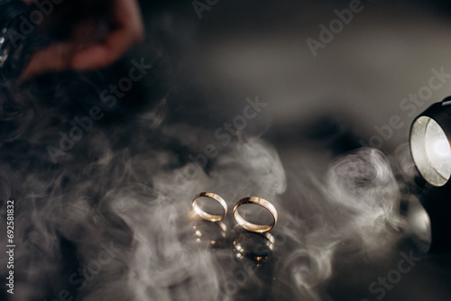 Two golden wedding rings with white smoke around, copy space and black background