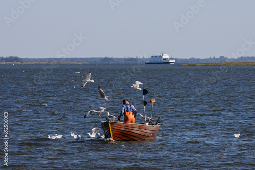 Fischer im Boot mit Möwen mit Fähre auf dem Bodden vor Hiddensee. photo