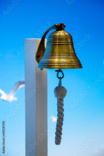 A sea bell or a rynda hanging on a wooden pole against a background of blue sky and seagulls. Ship sea ocean gear. photo