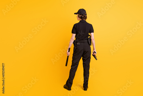 Full size rear portrait of police woman standing arms hold pistol baton isolated on yellow color background photo