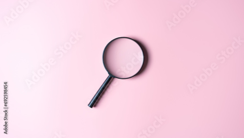 Close up of a black magnifying glass on a pink background. Top view with copy space. Finding or searching for ideas, explore for knowledge, find out. Magnifier finds answer. Science research concept.
