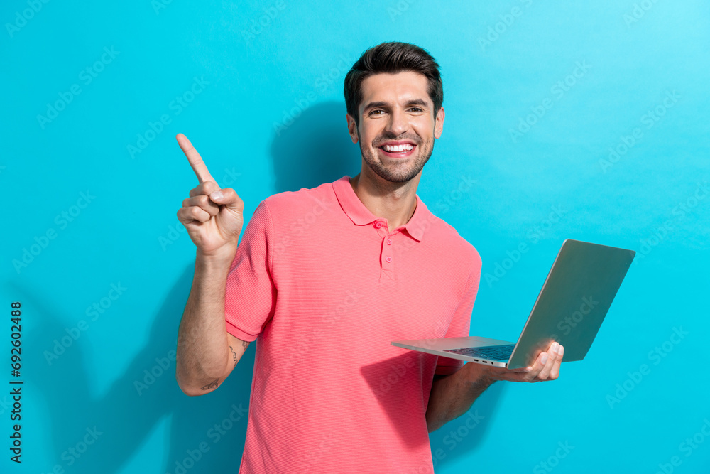 Portrait of young guy in pink t shirt works at office point finger empty space with netbook software ad isolated on blue color background Portrait of young guy in pink t shirt works at office point finger empty space with netbook software ad isolated on blue color background