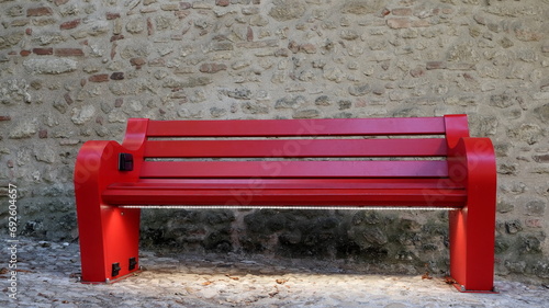 Panchina smart rossa situata nel centro storico.  Panchina interattiva di legno. Un muro di pietra antica come sfondo. photo