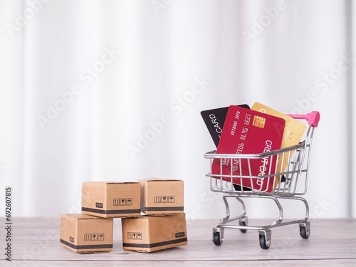 Credit cards in shopping cart and carton boxes on the table with white curtain background.
