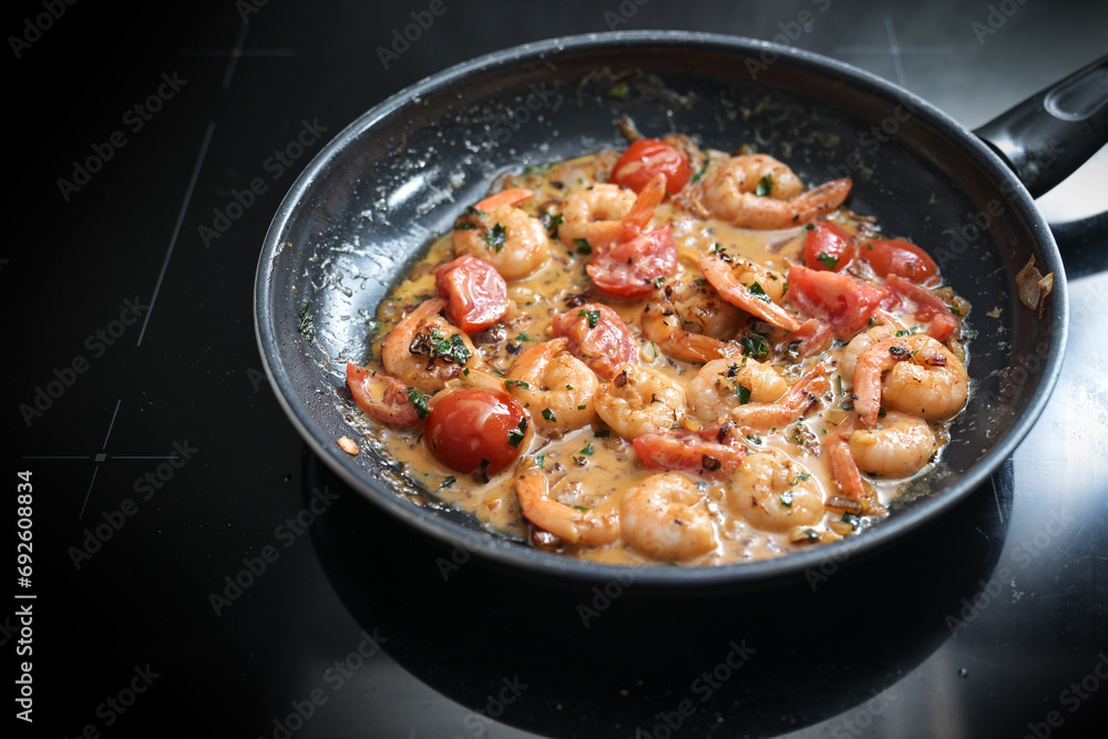Shrimps in tomato cream sauce sauteed with herbs, onions and garlic in a black frying pan on the stove top, cooking a Mediterranean seafood meal, selected focus Shrimps in tomato cream sauce sauteed with herbs, onions and garlic in a black frying pan on the stove top, cooking a Mediterranean seafood meal, selected focus