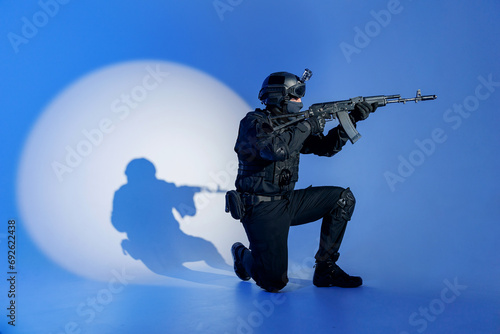 Action photo, Soldier in black uniforms with weapon standing on his knee in studio. Concept Military warrior army tactical force to fight crime in city