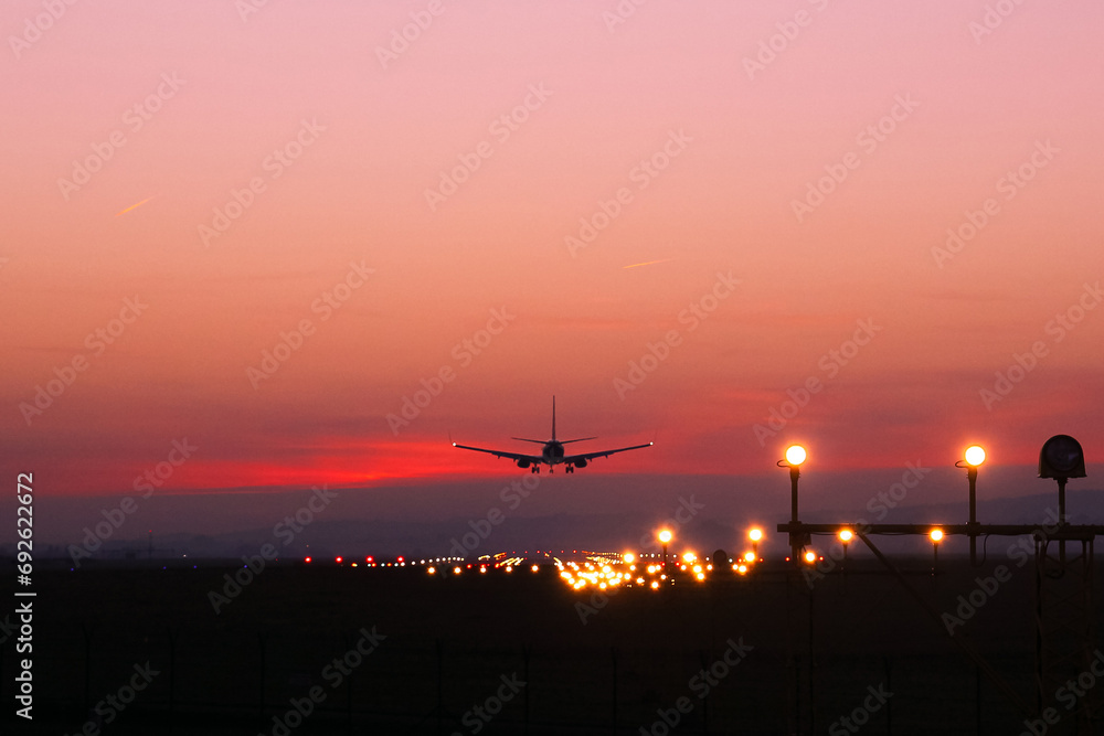 Plane lands at an airfield on the background of red clouds Plane lands at an airfield on the background of red clouds