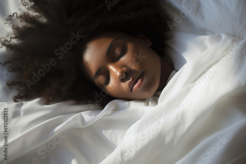 Peaceful young woman sleeping soundly, wrapped in soft white sheets, her curly hair fanned out, in a tranquil, sunlit room