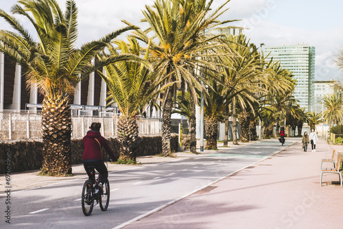 Young girl on bike rides on the bike path, on the background of palm trees and large houses, the concept of active recreation and sports