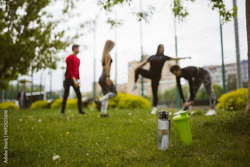 People do sports exercises on meadow focus on water bottles in grass. Active lifestyle equipment. Containers for drinks outdoors